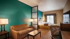 A hotel room with a teal accent wall, a sofa, a desk, a bed, and a television. - Best Western Plus Desoto Inn & Suites (Mansfield)