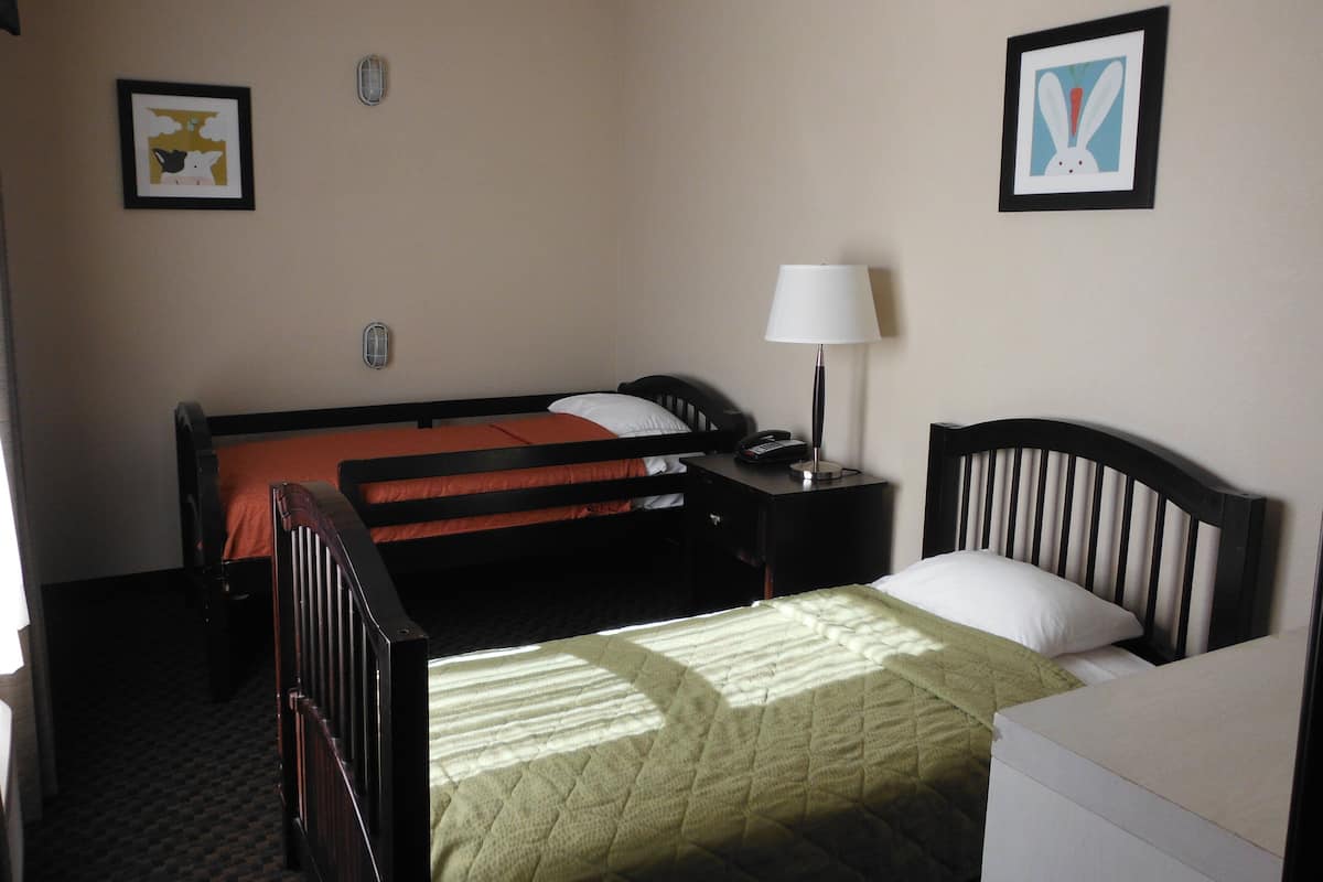 Habitación de hotel con dos camas, una mesita de noche con lámpara, teléfono y cuadros en las paredes.