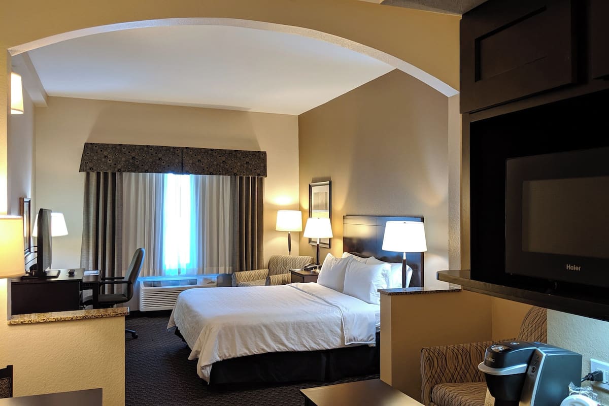 Una habitación de hotel con cama, escritorio, silla, lámparas y televisión.