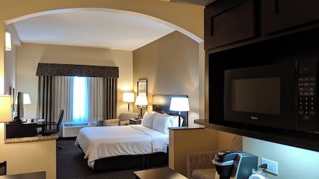 A hotel room with a bed, desk, chair, lamps, and a television.