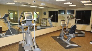 A hotel fitness center with cardio machines, free weights, and a mirrored wall.