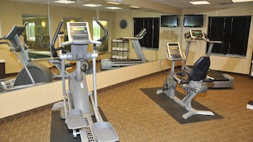 Une salle de sport d’hôtel équipée de machines de cardio, de poids libres et d’un mur avec des miroirs.
