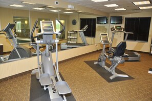 A hotel fitness center with cardio machines, free weights, and a mirrored wall.