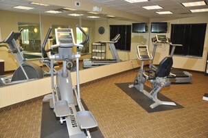 A hotel fitness center with cardio machines, free weights, and a mirrored wall.