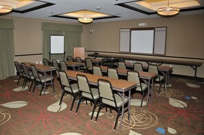 A conference room with tables and chairs, a projector screen, and a carpeted floor.