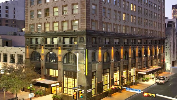 A multi-story hotel with a classic architectural design, featuring a prominent entrance with large windows and a covered area. - Home2 Suites by Hilton San Antonio Downtown - Riverwalk, TX (San Antonio)