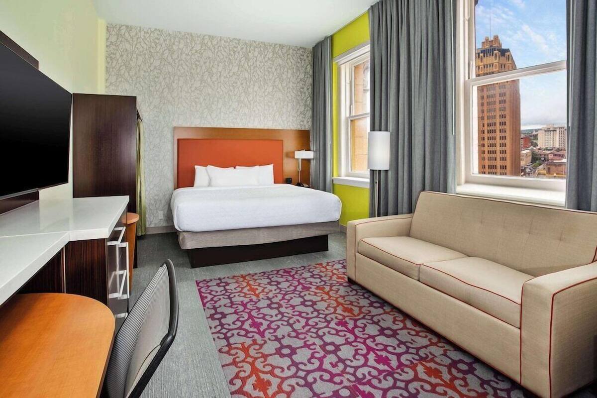 A hotel room with a bed, a sofa, a desk, and a TV.