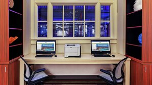A workspace with two computers, a large window with blue lighting, and a view of the cityscape. - Home2 Suites by Hilton San Antonio Downtown - Riverwalk, TX (San Antonio)
