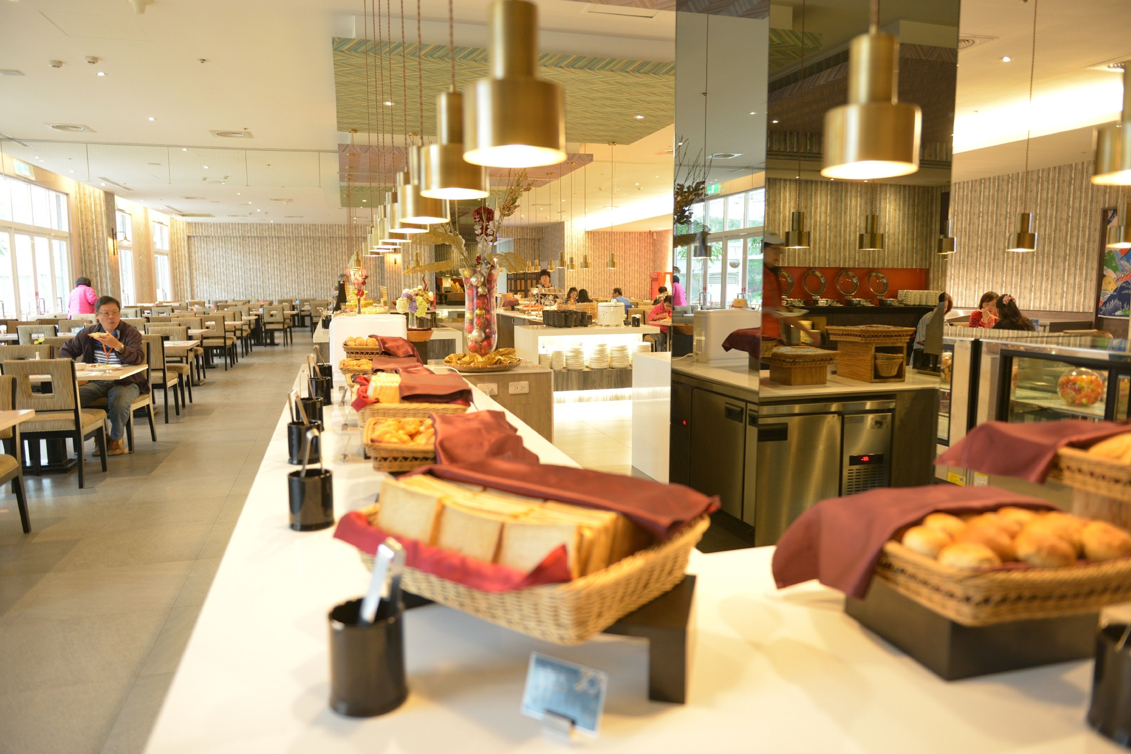 A spacious hotel dining area with multiple tables and chairs, a buffet setup with various food items, and a counter with a beverage station.