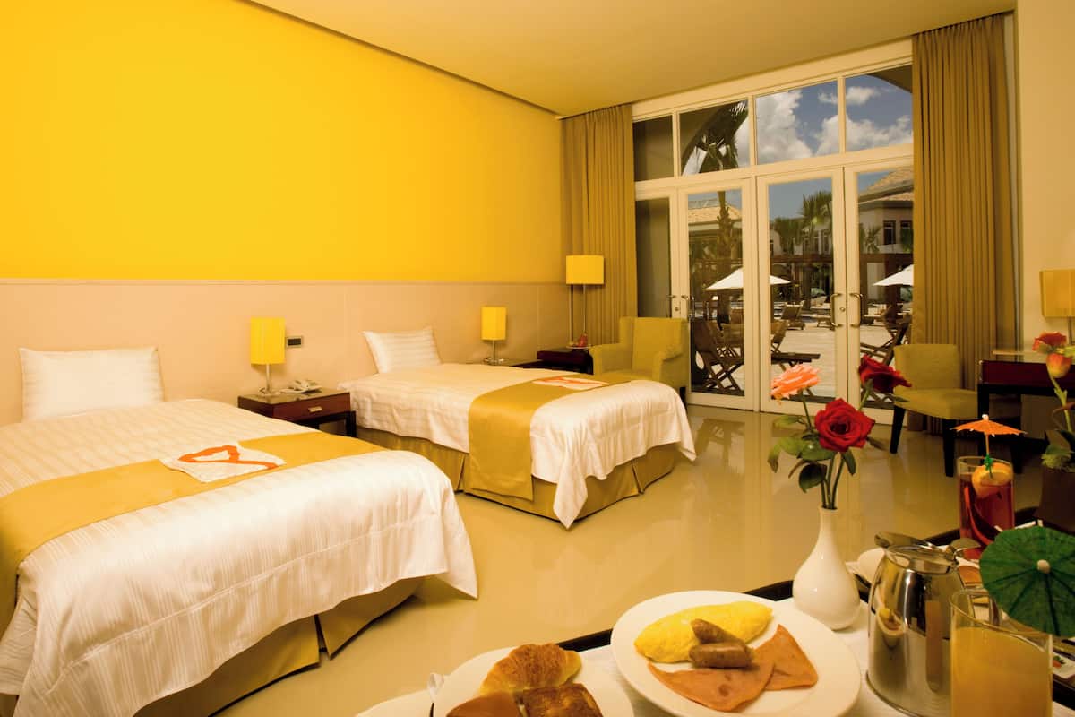 Habitación de hotel con dos camas, una mesa de comedor con desayuno y vistas al exterior.