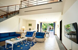 A spacious living area with a blue sofa, two armchairs, a coffee table, and a flat-screen TV. A staircase leads to an upper level.