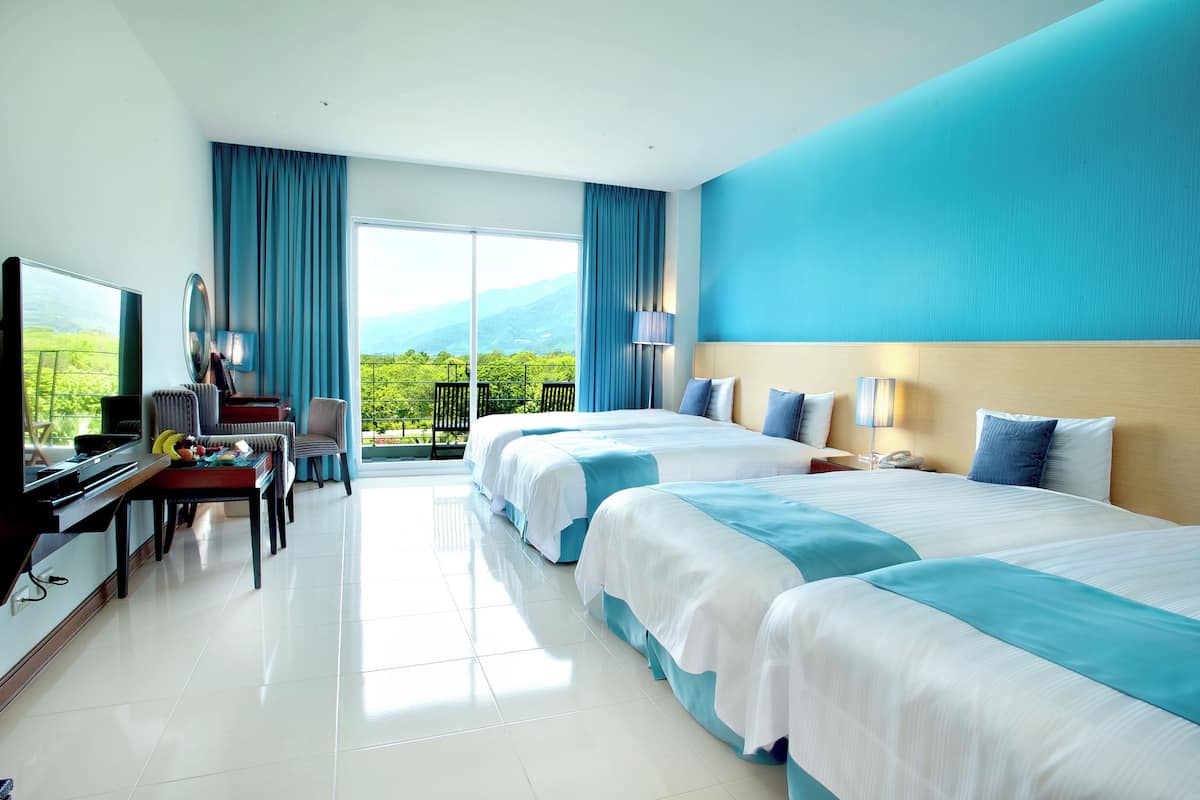 Habitación de hotel con dos camas, televisión, escritorio y balcón con vistas a las montañas.