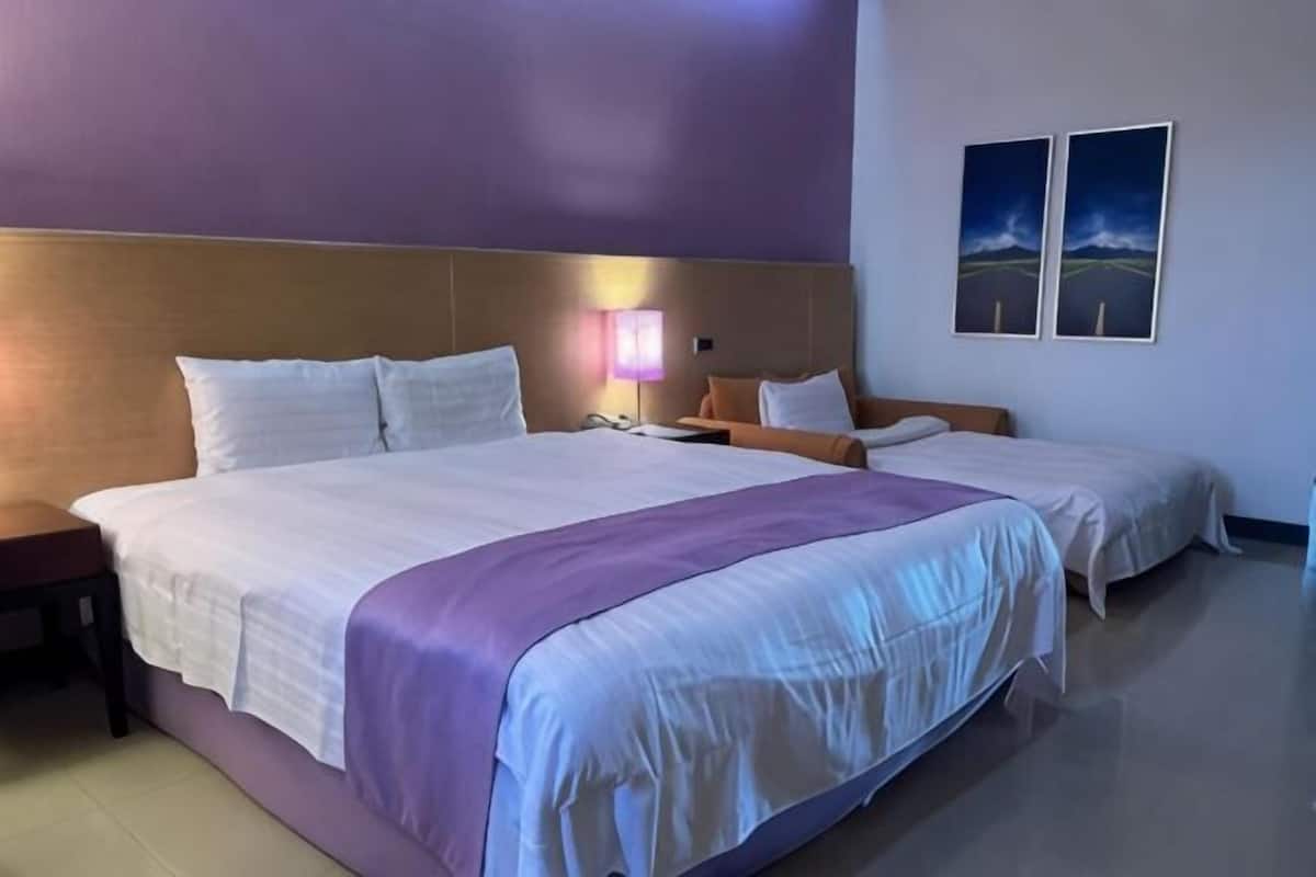 Habitación de hotel con una cama grande, una mesita de noche, una lámpara y dos cuadros en la pared.