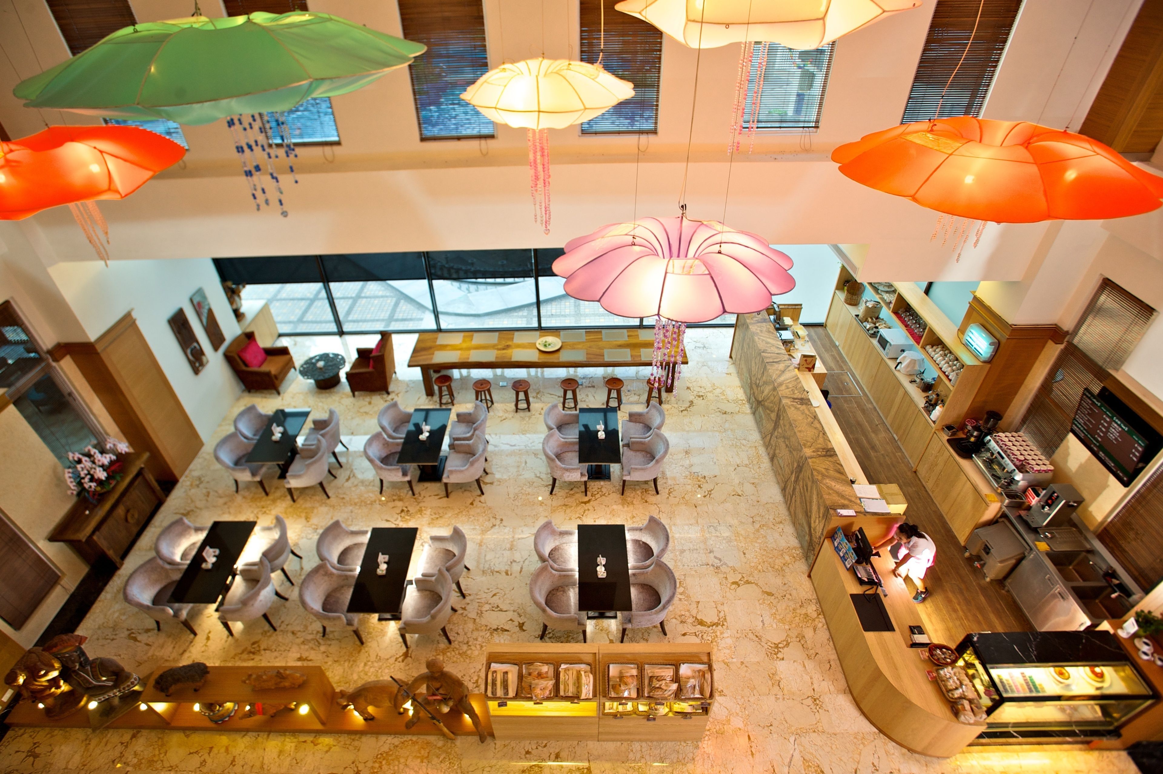 Un hall d’hôtel spacieux, doté de nombreuses tables et chaises, d’un comptoir de réception et de plusieurs parasols décoratifs suspendus au plafond.