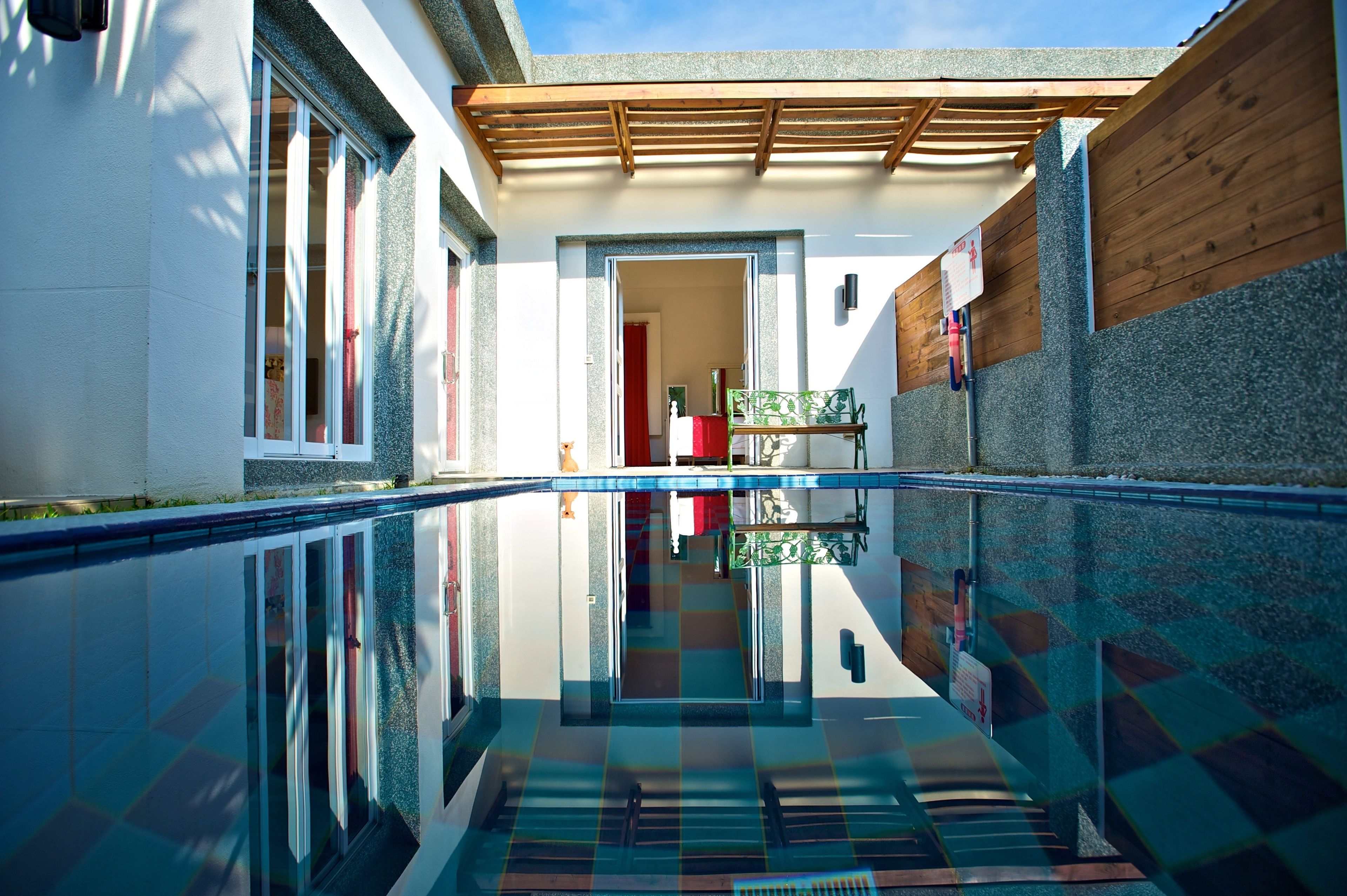 A clear pool with a tiled floor and a wooden pergola overhead.