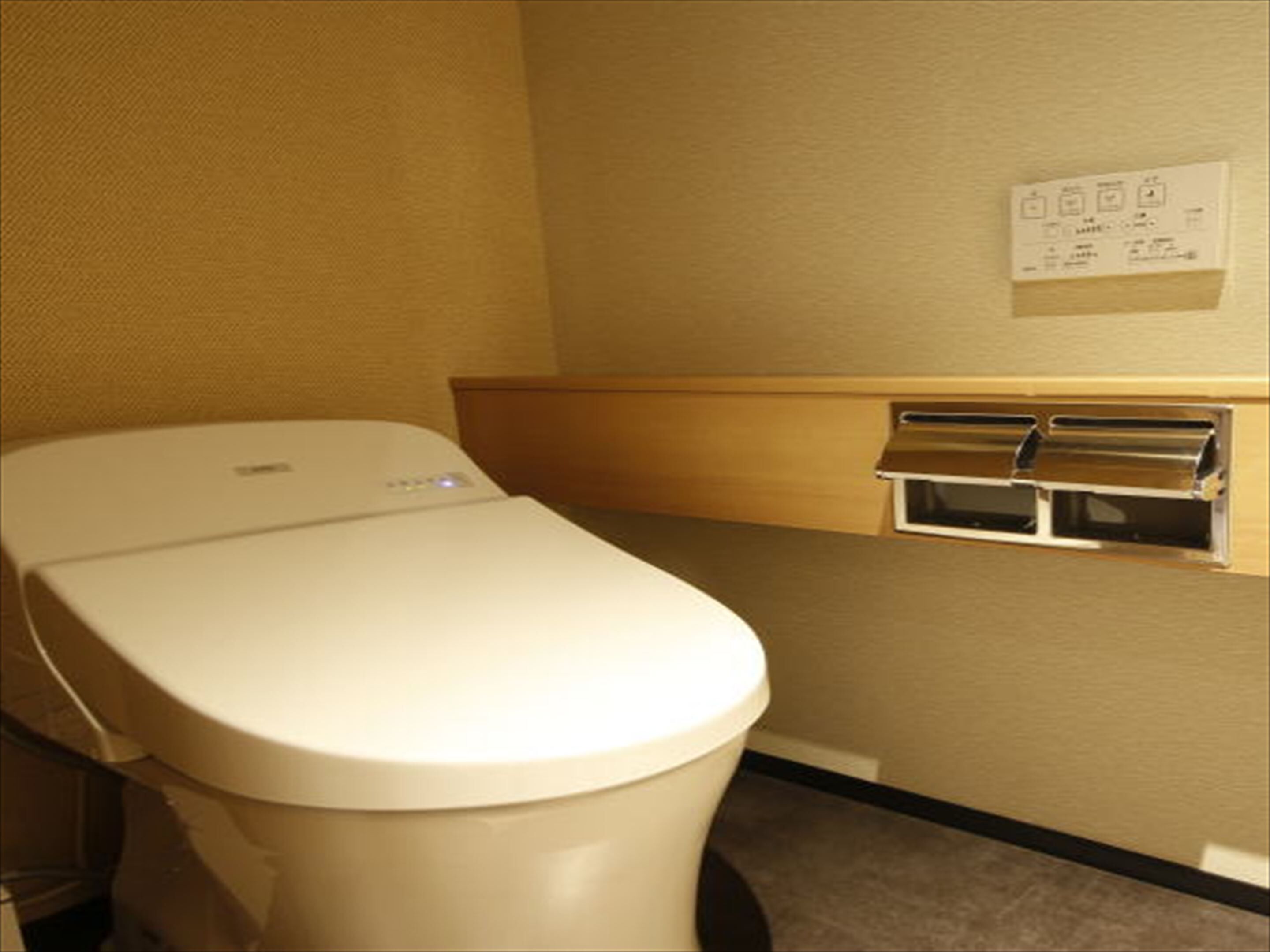 Des toilettes dotées d’un panneau de commande, d’un distributeur de papier fixé au mur et d’une petite étagère.