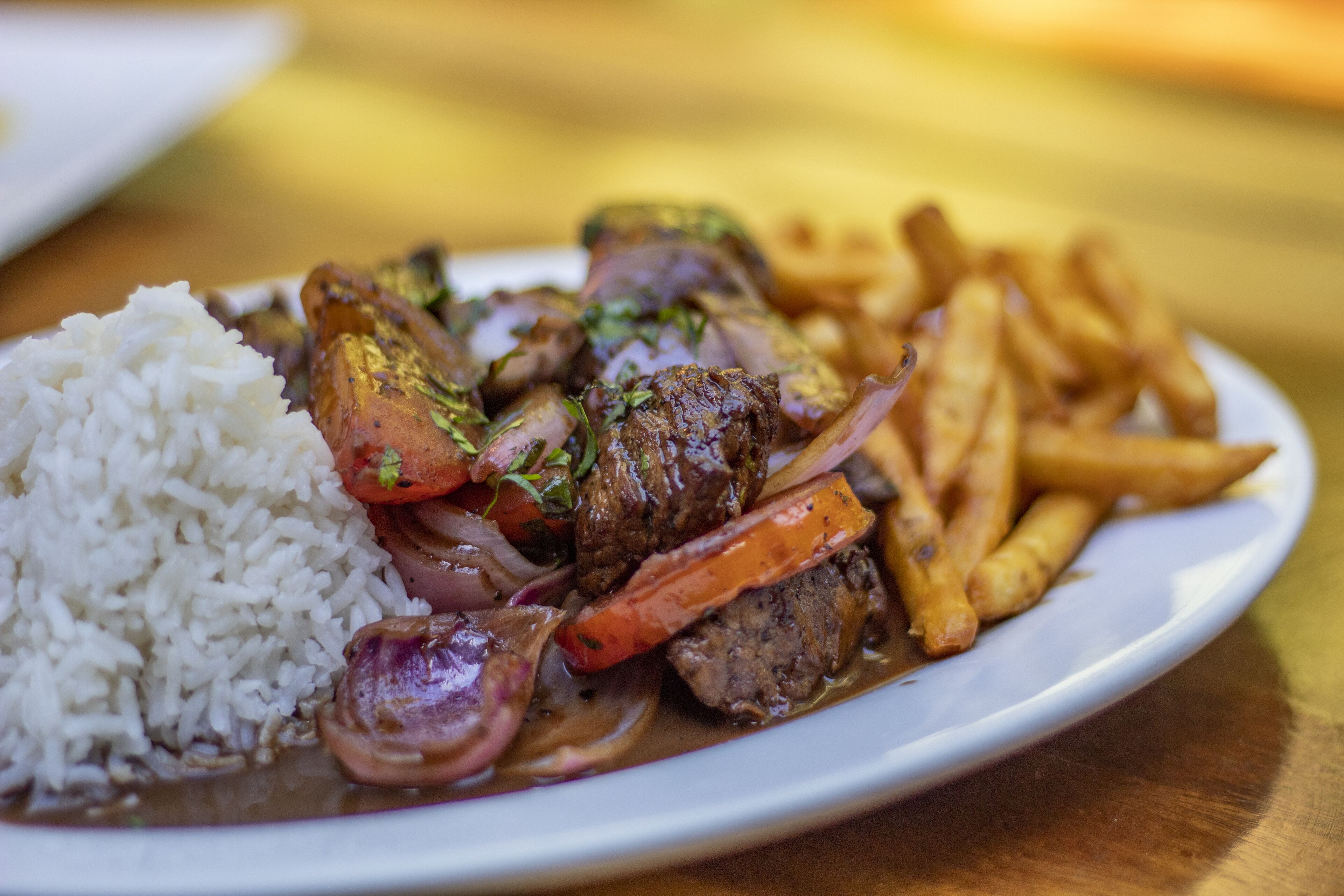 A plate with white rice, beef, carrots, and red onions, accompanied by French fries.