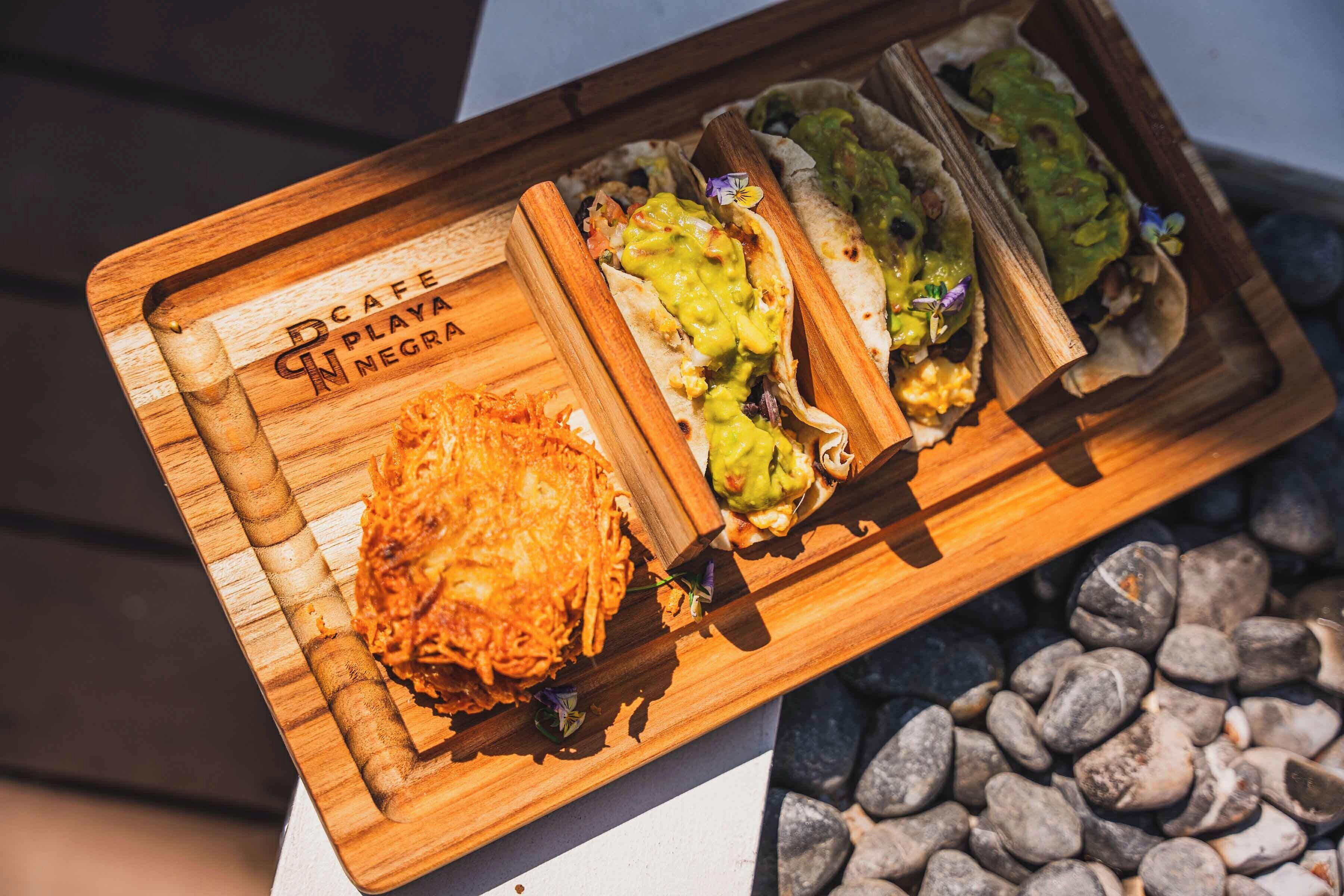 Un plateau de service en bois contenant trois tacos et un plat frit, probablement une collation ou un dessert.