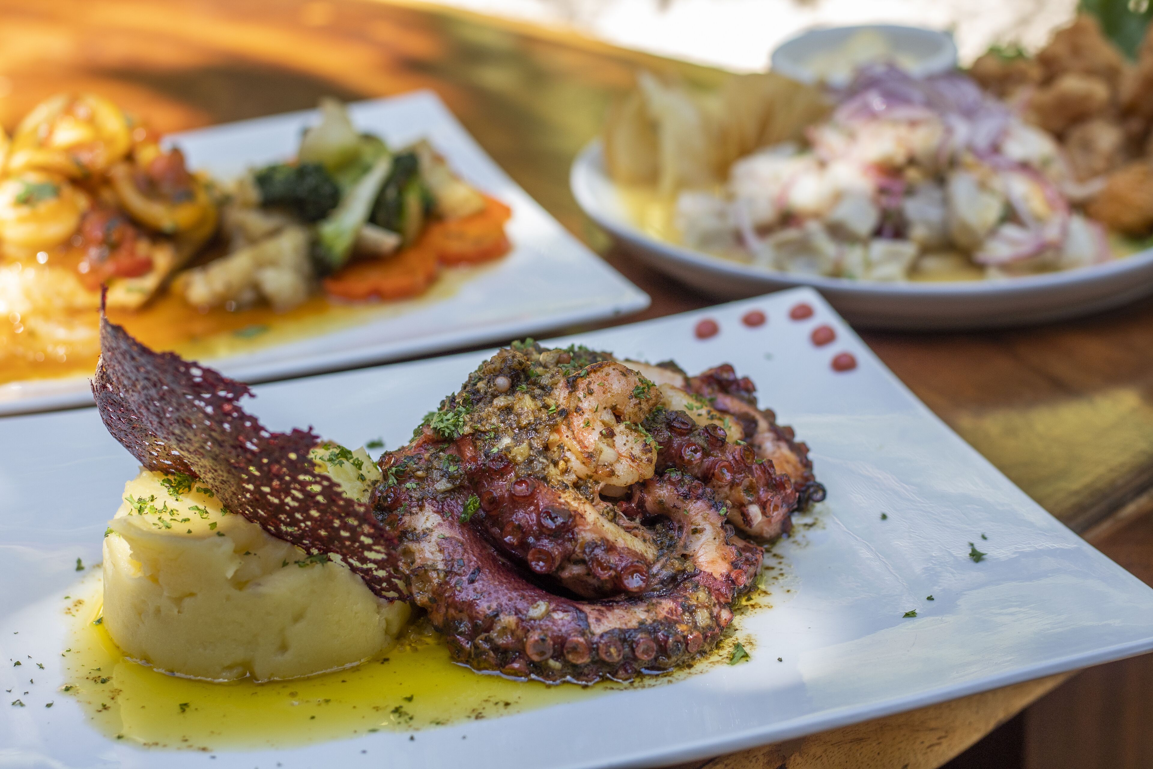 A dining table with plates of food, including octopus and potatoes.