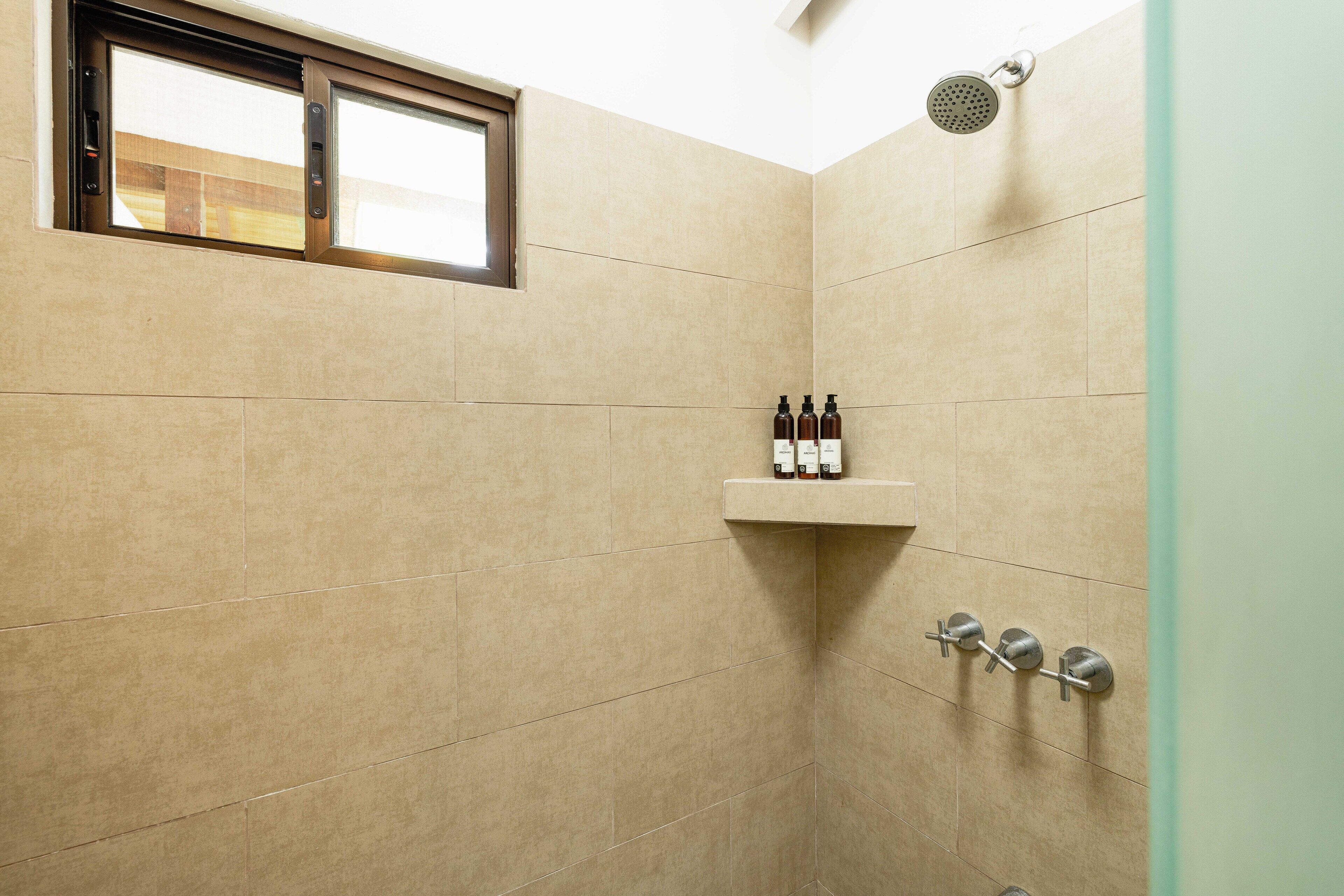 A modern shower with a window, a shelf with toiletries, and a rain showerhead.