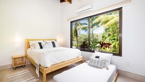 A bedroom with a large window, a bed, a bedside table, and a small nightstand.