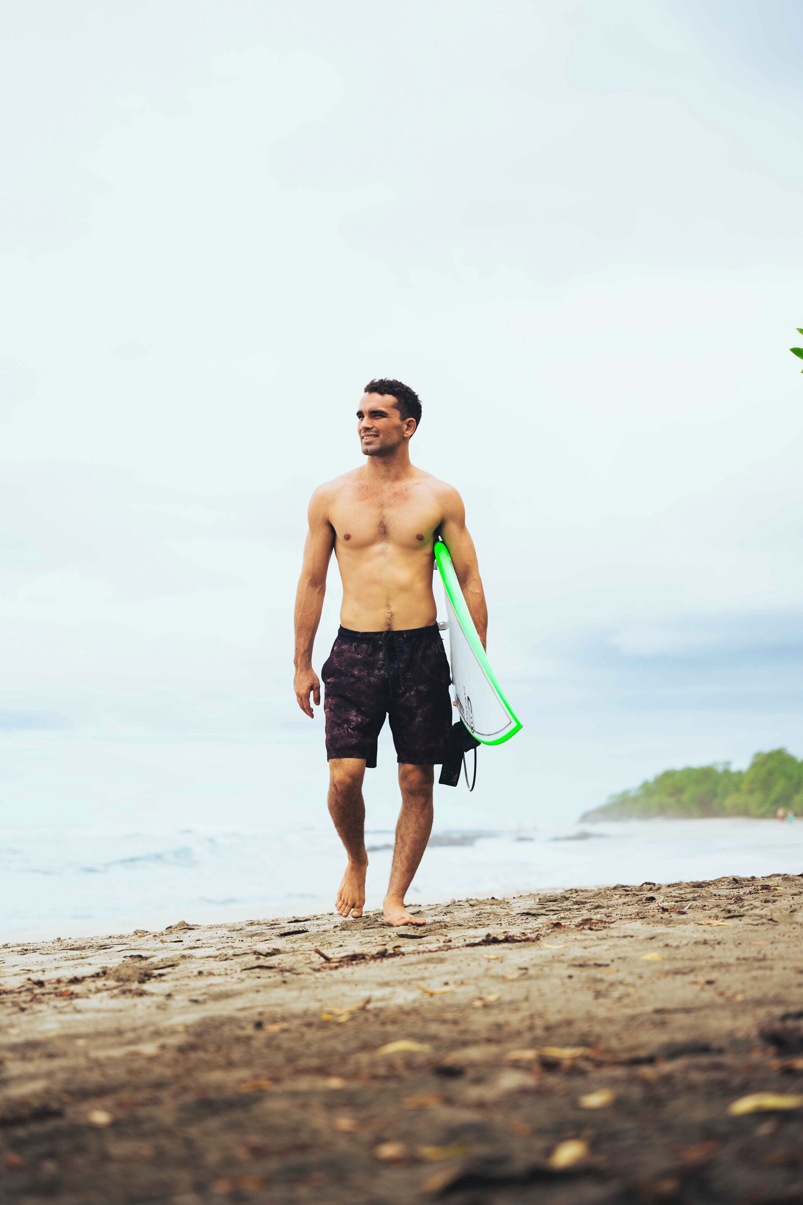 Eine Person geht am Strand und trägt einen Surfbret.