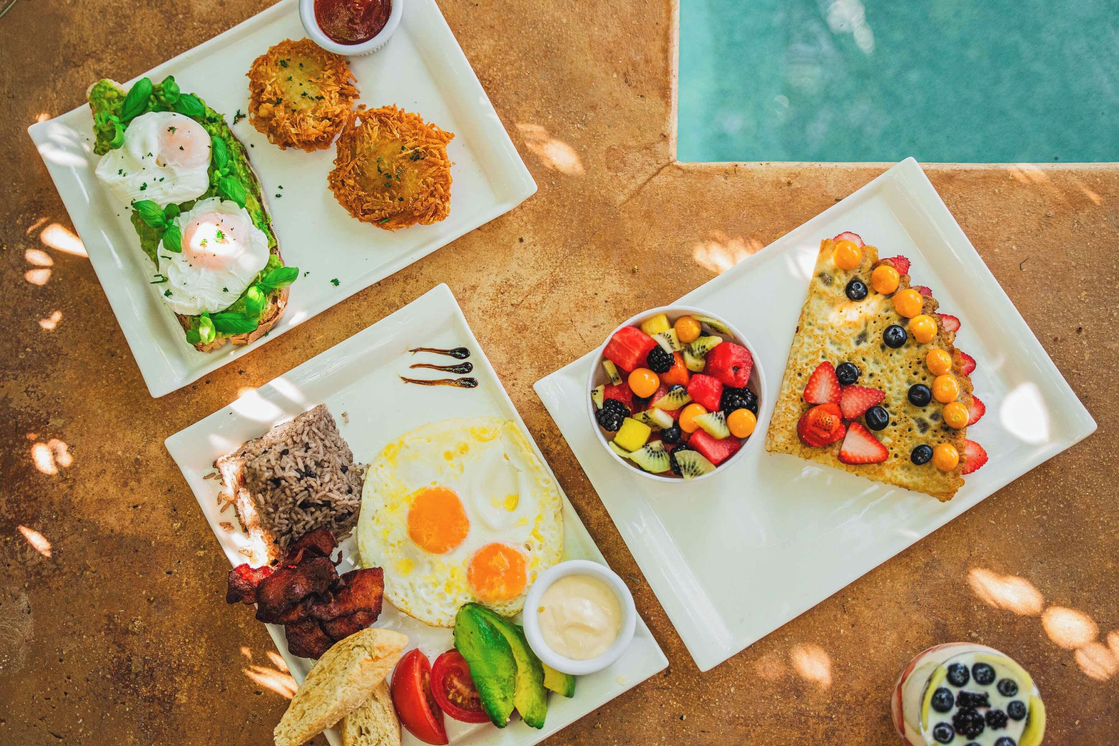 A table with breakfast plates including eggs, avocado, and fruit.