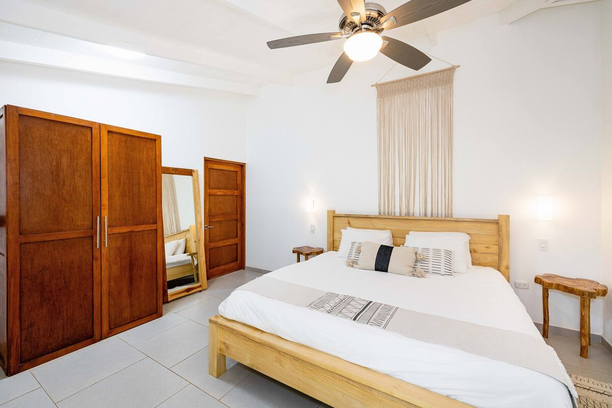 Ein Schlafzimmer mit einem hölzernen Bett, einem Deckenventilator, einem Kleiderschrank und einem Nachttisch.