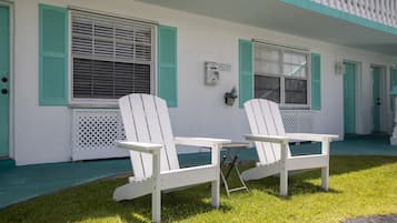 A white building with teal shutters, two white Adirondack chairs, and a small table.