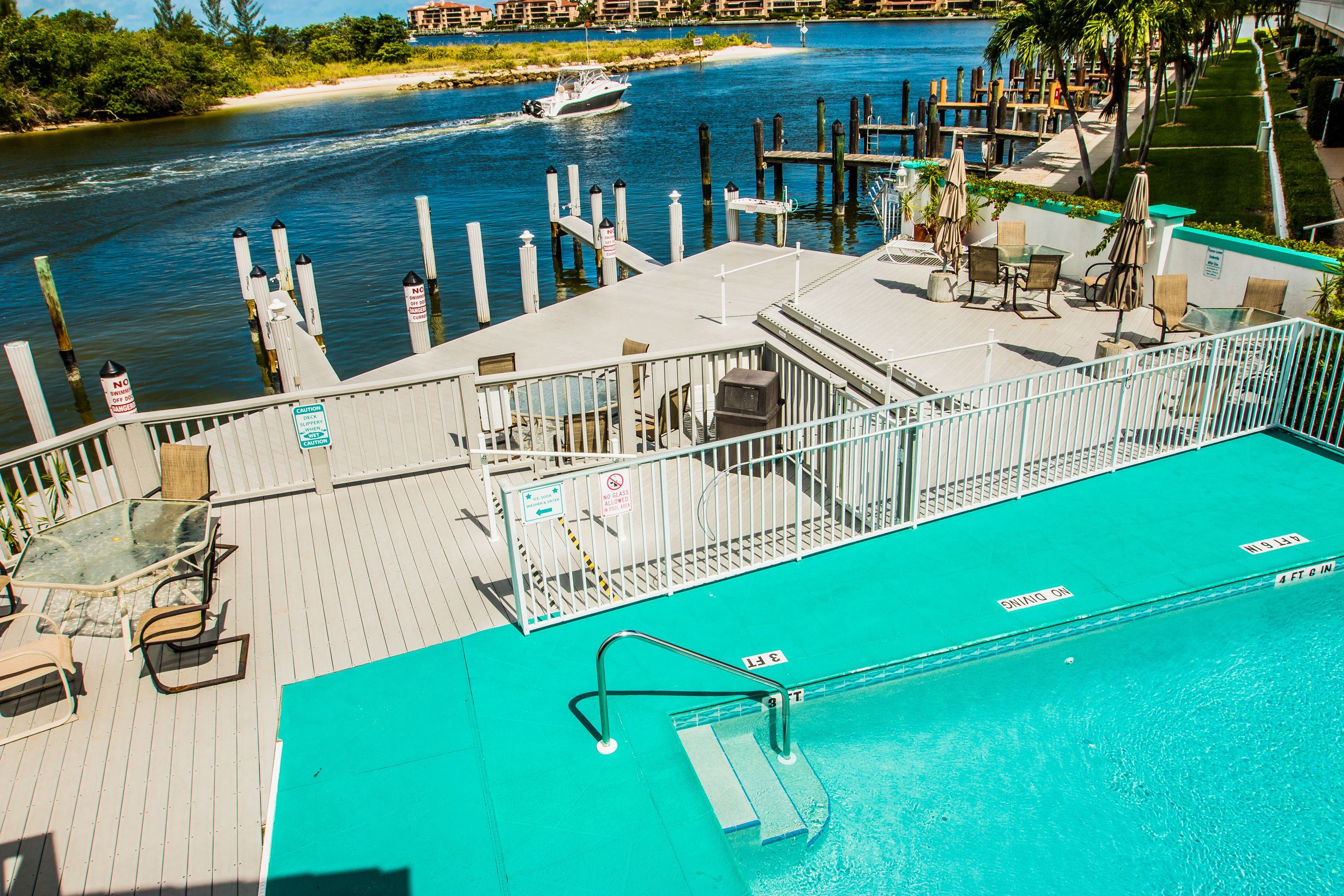 Zona de piscina con vista a un cuerpo de agua, barcos amarrados y mobiliario exterior.