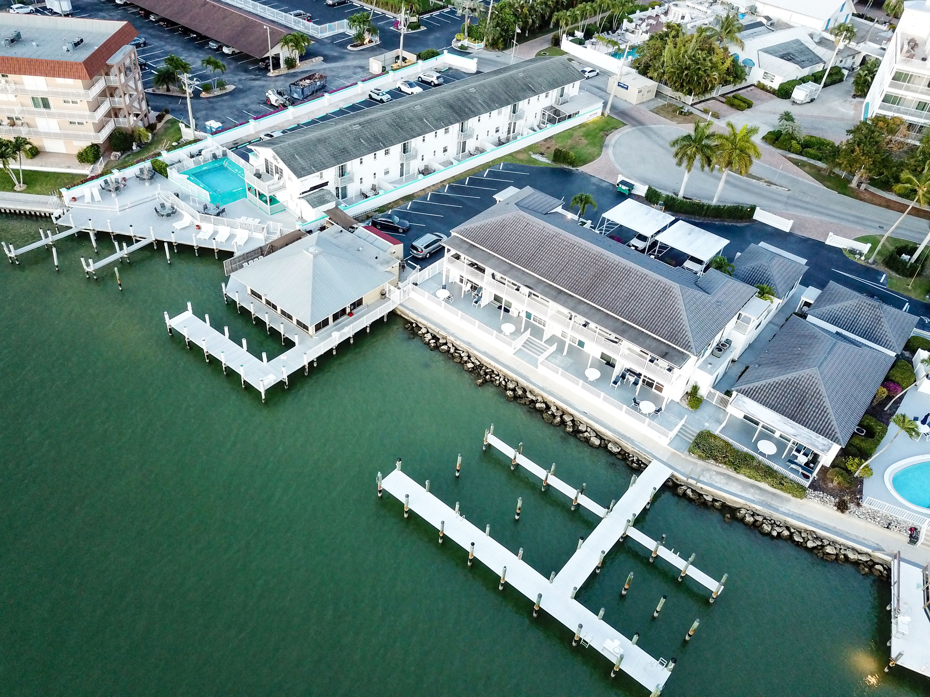 Luchtbeeld van een hotel aan het water met een zwembad, meerdere steigers en een groot gebouw met een overdekt terras.