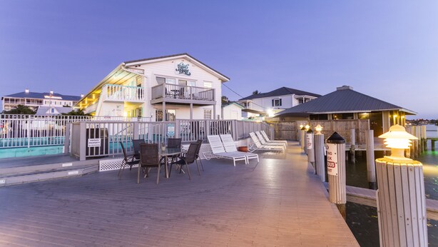 A wooden deck with lounge chairs and a table, a pool, and a building with a balcony. - The Boat House (Marco Island)
