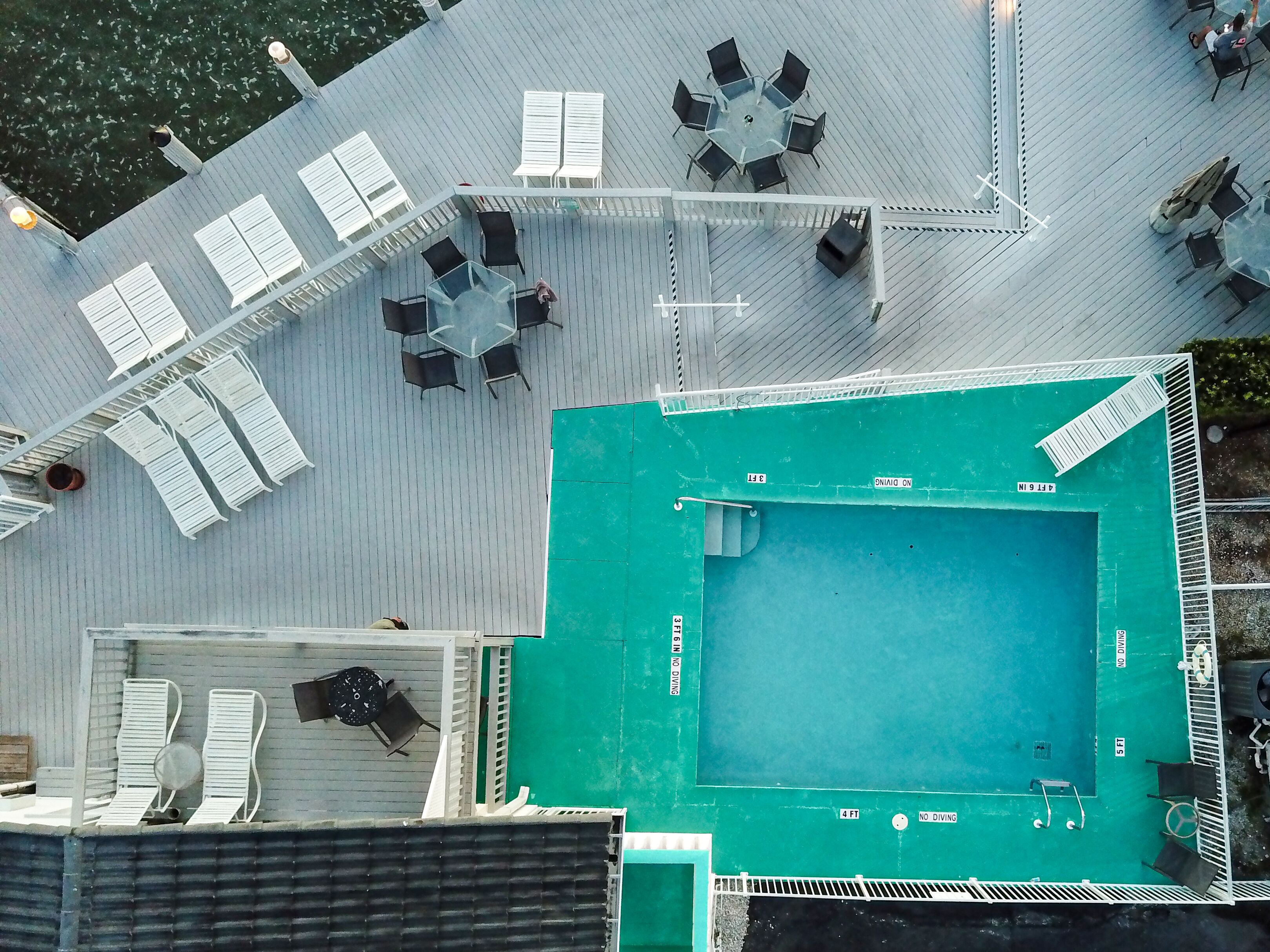A rooftop pool area with multiple lounge chairs and tables, a swimming pool, and a covered seating area.