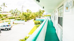 A hotel corridor with a green carpet, white walls, and a view of the street with cars and palm trees.