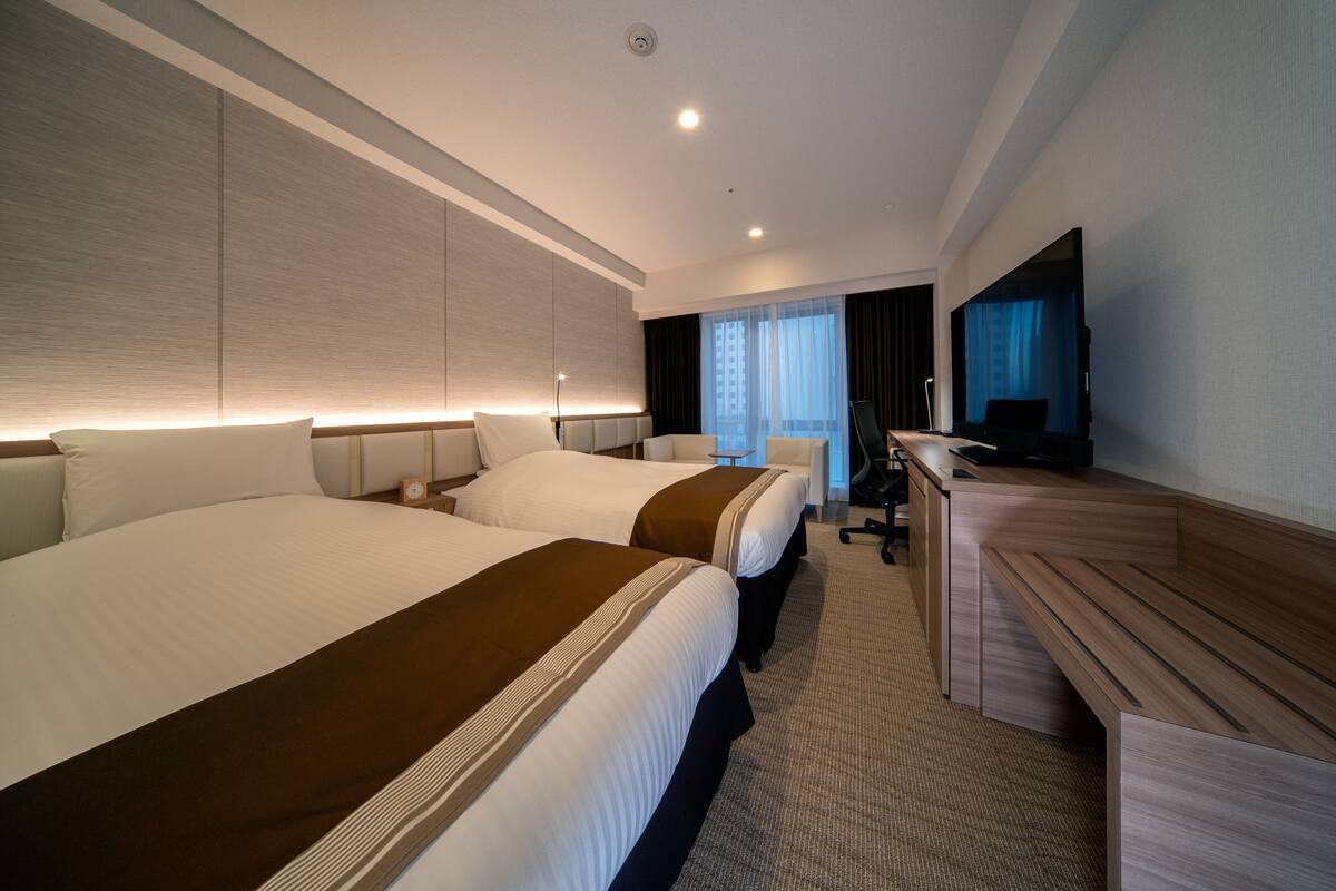 Une chambre d’hôtel avec deux lits, un bureau, une chaise et un téléviseur.