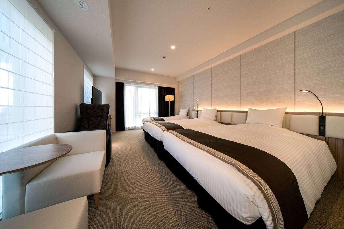 Une chambre d’hôtel moderne avec un grand lit, un canapé, un bureau et une grande fenêtre.
