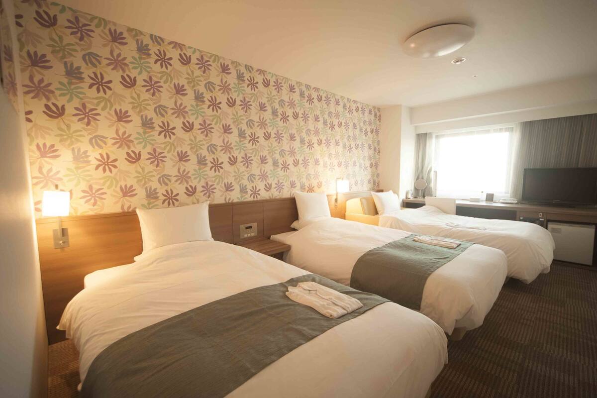 Une chambre d’hôtel avec deux lits, une télévision et un papier peint à motifs floraux.