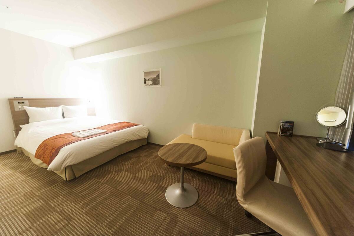 Une chambre d’hôtel avec un lit, une petite table ronde, un canapé et un bureau avec un miroir.