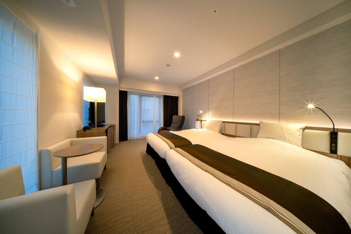 Une chambre d’hôtel moderne, dotée d’un grand lit, d’un bureau, d’une chaise et offrant une vue sur l’extérieur.