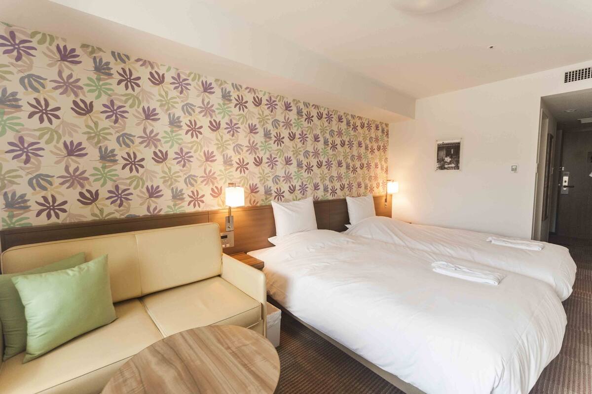 Une chambre d’hôtel comprenant un lit, deux tables de chevet, un canapé et une petite table ronde.