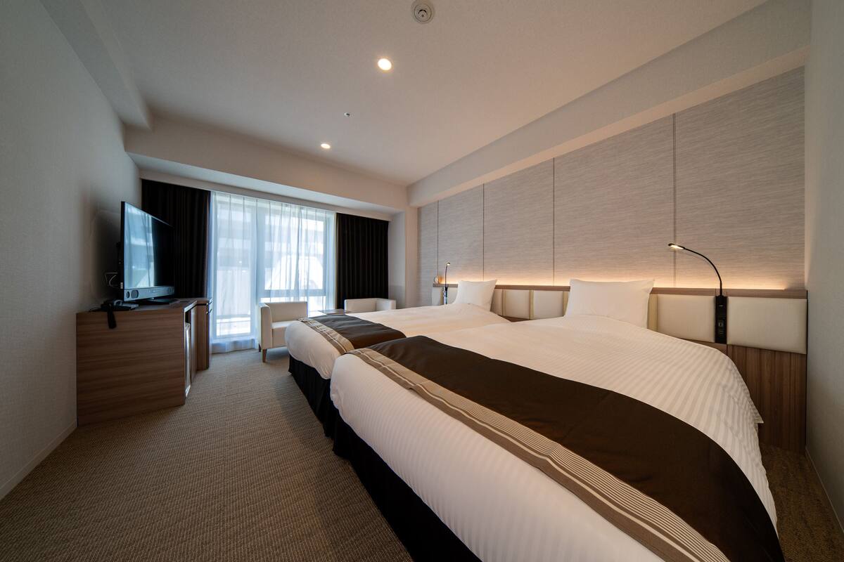 Une chambre d’hôtel avec un grand lit, un bureau, une télévision et une fenêtre avec des rideaux.