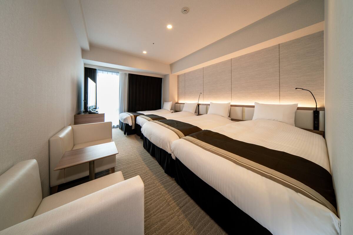 Une chambre d’hôtel avec un grand lit, deux tables de chevet, un canapé et une fenêtre avec des rideaux.