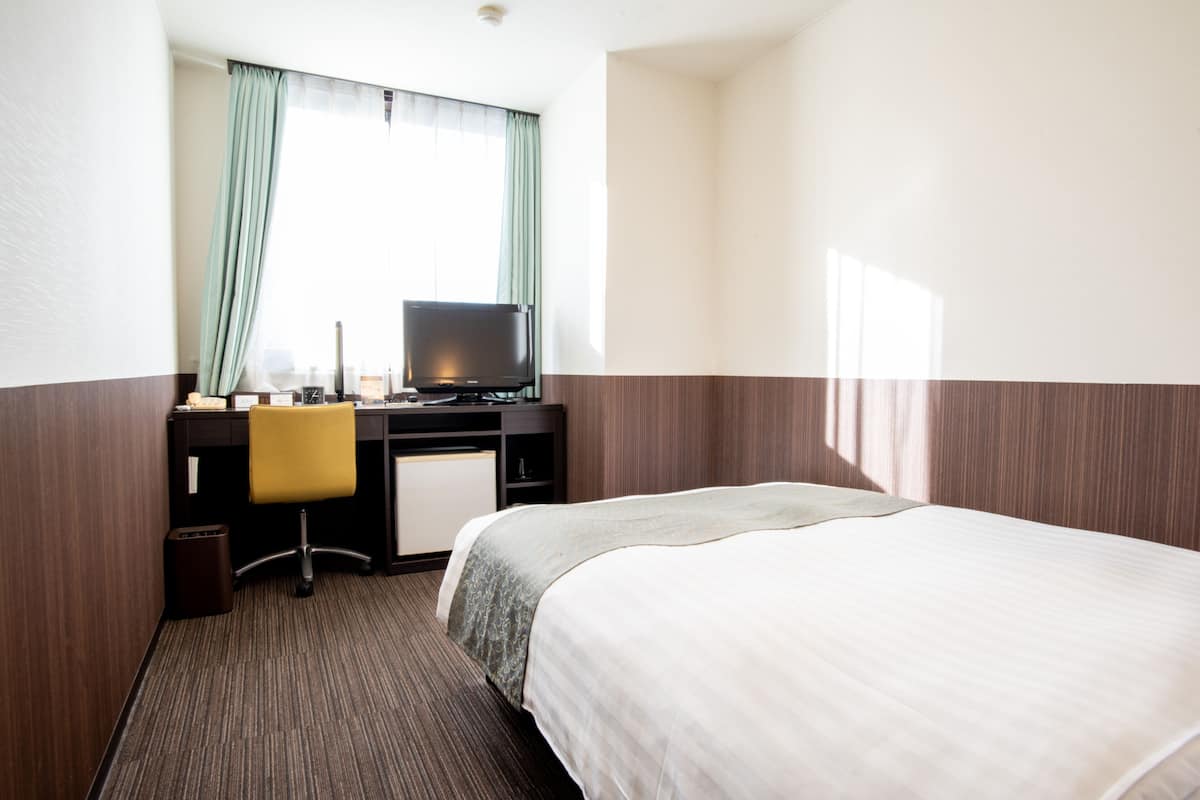 A hotel room with a bed, a desk with a computer, a chair, and a television.