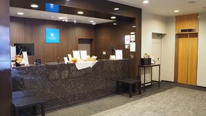 Un comptoir d’accueil d’hôtel avec un plan de travail en marbre, un petit banc et un panneau indiquant la présence d’un défibrillateur automatisé externe (DAE), fixé au mur.