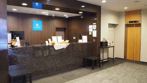 Zona de recepción de un hotel con mostrador de mármol, una pequeña mesa con un ordenador portátil y un mostrador de recepción.