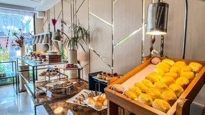 Monipuolinen aamiaisbuffet, jossa on tarjolla erilaisia leivonnaisia ja leipää, kahvilaitteet sekä näkymä ulos.