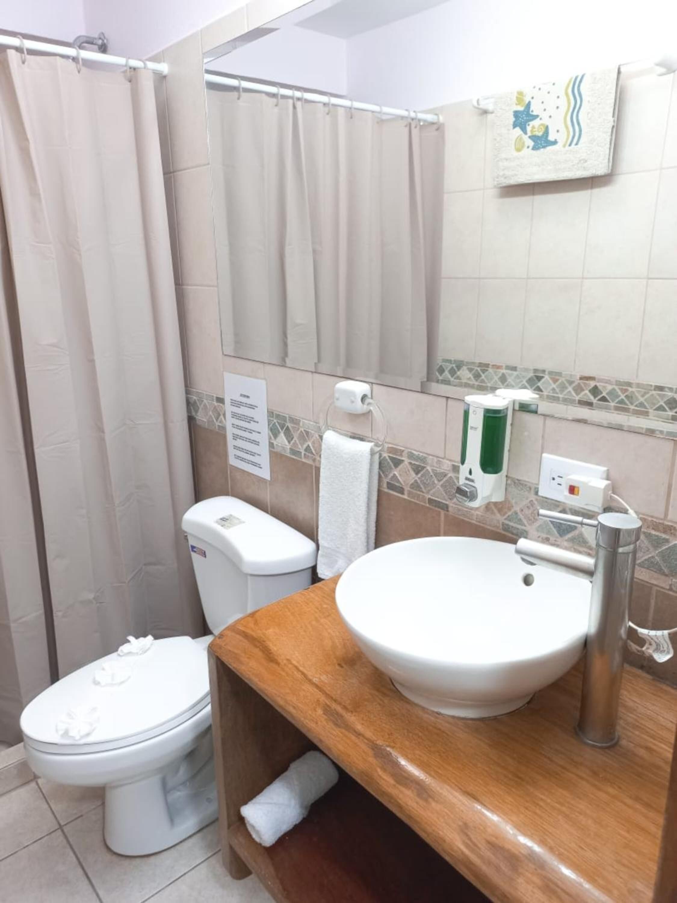Un baño con inodoro, lavabo, cortina de ducha, toallero y dispensador de jabón.