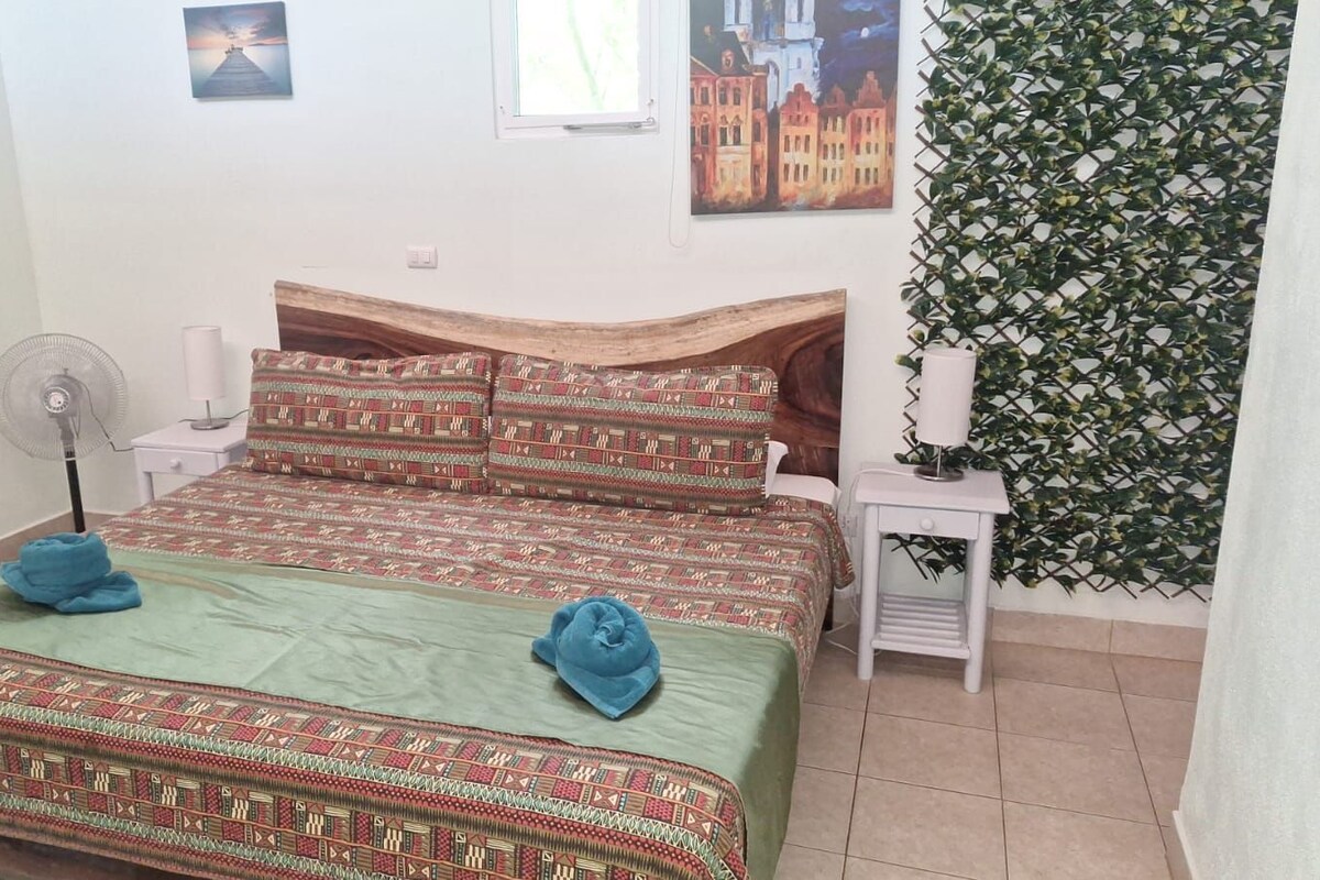Una habitación con dos camas, un ventilador, una mesita con lámpara y una pared con un estampado de hojas.