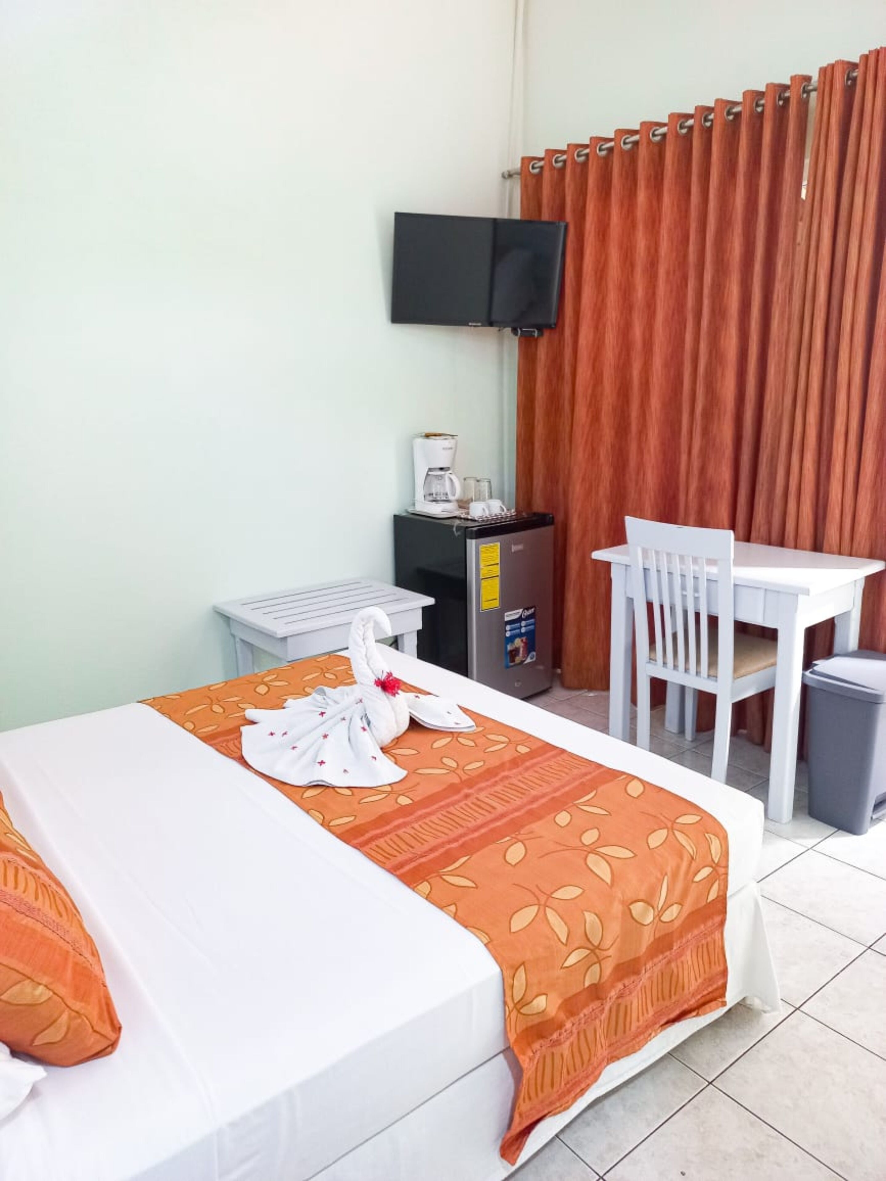 A hotel room with a bed, a desk, a chair, a coffee machine, and a TV on the wall.