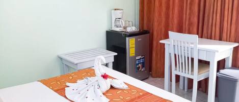 A hotel room with a bed, a desk, a chair, a coffee machine, and a TV on the wall.